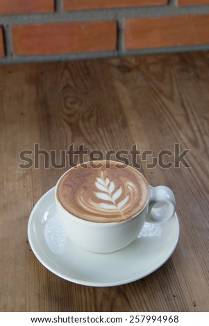 A cup of coffee with leaf pattern in a white cup on wooden background.