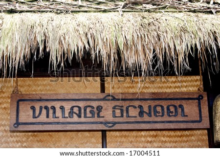 Sign in Thai style writing hanging from a grass hut.