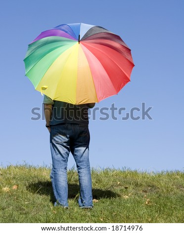 A person standing alone, watching the horizon, with a rainbow coloured umbrella.