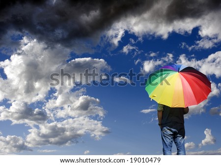A person standing alone, watching a storm approach, with a rainbow colored umbrella.