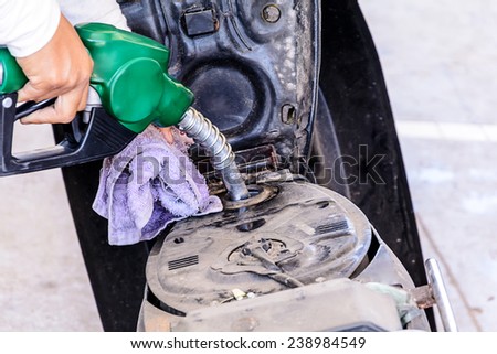 Closeup of hand fuel nozzle in pouring to motorcycle at gas station.