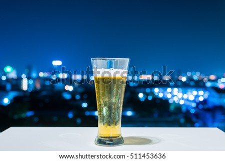 Glass of beer on white table of City at night background.