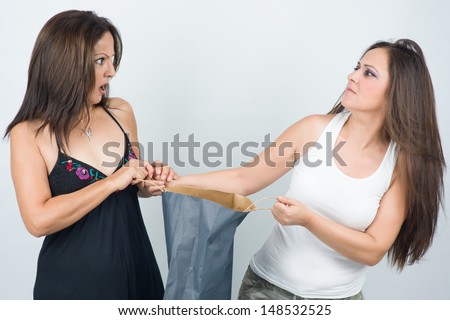 Two women fighting over shopping bag with furious expressions