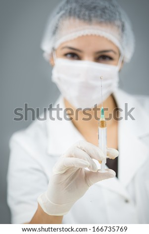 Smiling doctor with gloves mak and cap holding syringe with colorful injection