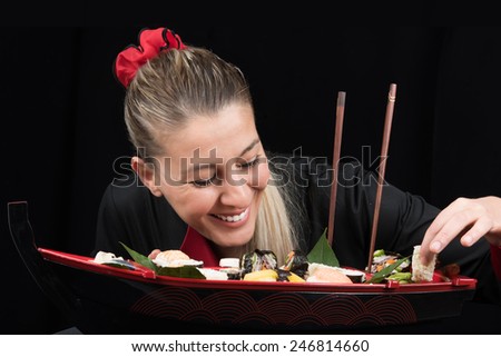 Young woman cook in uniform preparing luxury boat shaped sushi dish while smiling
