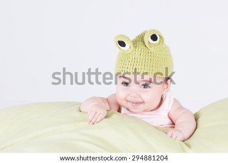 Little baby with frog hat smiling and looking up on pillow