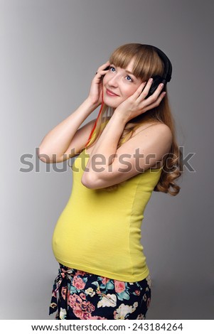 Pregnant woman listening to music on headphones. Pregnant woman enjoying music. Bright, beautiful girl in studio