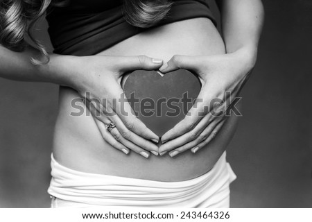 Close up on pregnant belly. Woman expecting a baby holding a red heart with love.  heart shape, fingers Heart symbol.  Black and white photo. Heart with love.