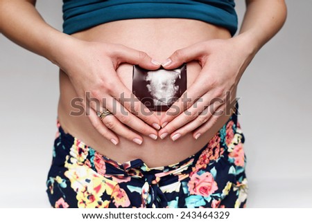 Close up of pregnant woman holding ultrasound scan on her tummy. photo of pregnancy, pregnant woman, family, parenthood, motherhood. ultrasound scan on her belly
