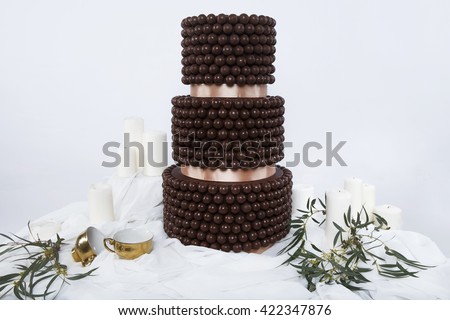 Wedding cake decorated with  greens costs on a white table decorated greece style with white  walls and gold cups. Delicious  chocolate wedding cake with sweet candy. olive branch