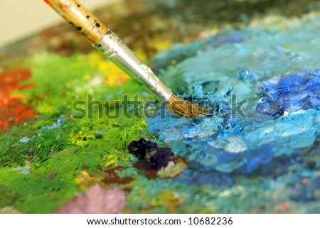 big paintbrush is mixing colors on palette. Shallow DOF