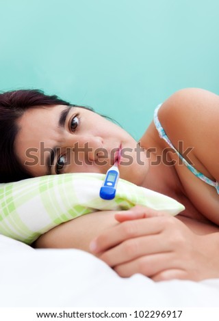 Beautiful hispanic woman sick in bed with a thermometer in her mouth