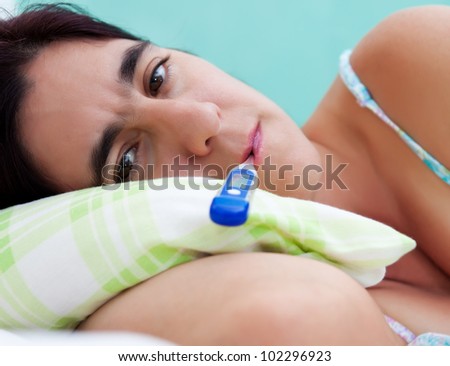 Close-up portrait of an hispanic woman sick in bed with a thermometer in her mouth