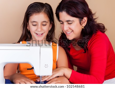 Happy hispanic mother teaching her daughter how to use a sewing machine
