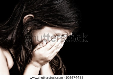 Dramatic grunge portrait of a girl crying with her hands on her face isolated on a black background