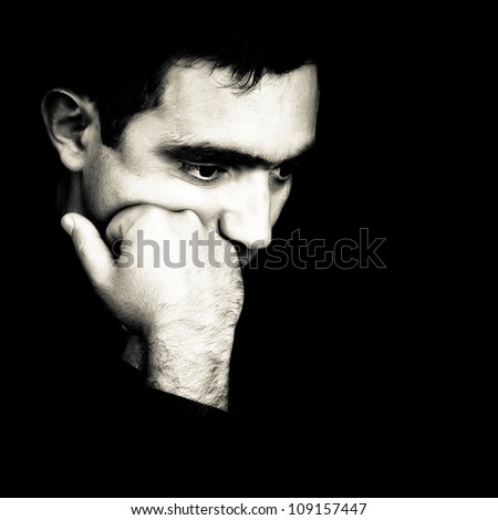 Black and white  dramatic close-up  of a man thinking with a fist on his chin emerging from a black background