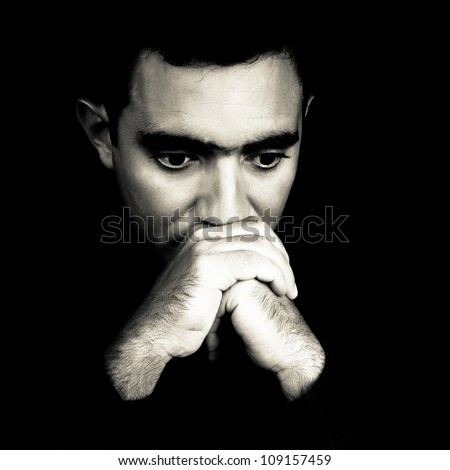 Dramatic black and white face of a worried young man  emerging from a black background