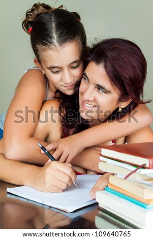 Young hispanic woman working or studying at home while her daughter hugs her from behind