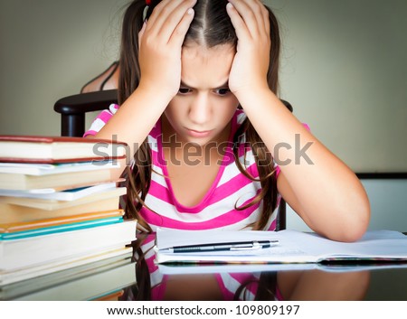 Angry and tired schoolgirl studying with a pile of books on her desk