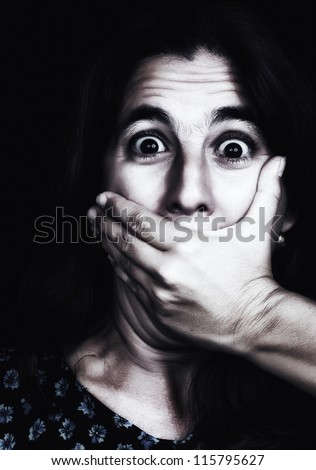 Grunge image of a frightened woman covering her mouth useful to illustrate gender violence or discrimination (on a black background)