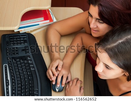 Hispanic girl and her young mother using a computer at home wit books on the computer desk (Image taken from above)