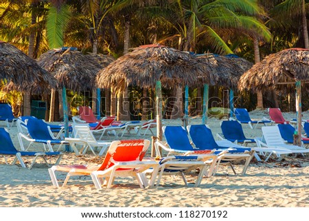 Umbrellas and beds next to coconut trees on the beach of Varadero in Cuba at sunset