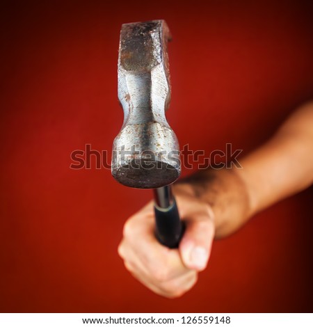 Hand holding a hammer on a bright red background (useful to illustrate the concept of strength or impact)