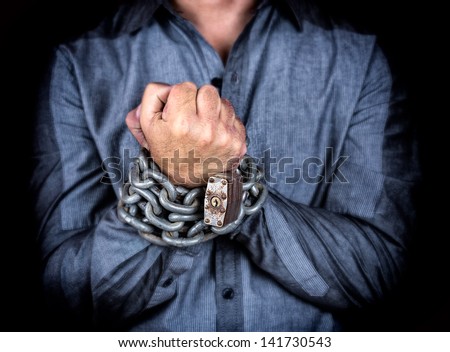 Hands of a formally dressed man chained with an iron chain and a padlock (on a black background)