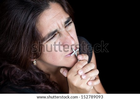 Emotional portrait of an hispanic woman praying and kissing a small crucifix (isolated on black)