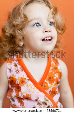 Portrait of a beautiful baby girl with beautiful blue eyes smiling on a colorful orange background