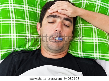 Sick hispanic man laying in bed with fever while a woman\'s hand touches his forehead