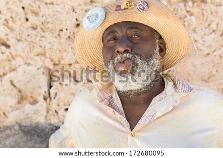 HAVANA,CUBA - JANUARY 20, 2014:Afrocuban man smoking a cigar near the Cathedral Square.Characters like this are common in Old Havana and a photo opportunity for the growing number of foreign tourists