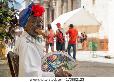 HAVANA,CUBA - JANUARY 20, 2014:Old black lady smoking a huge cuban cigar next to the havana Cathedral.Characters like this are a common sight in the streets of Old Havana