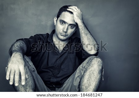 Grunge desaturated  image of a stressed and worried young man sitting on the floor isolated on a black background