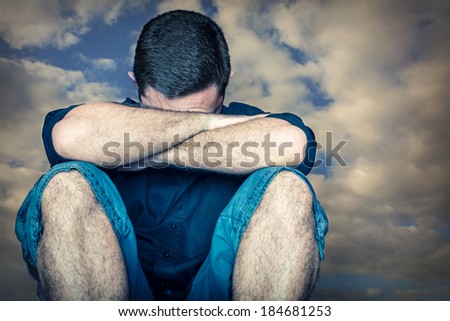 Sad young man hiding his face and crying with a stormy clouds background
