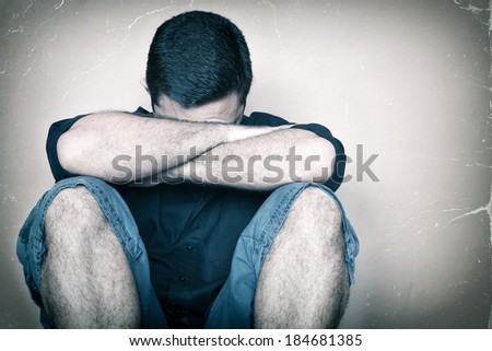 Very sad young man sitting on the floor crying and hiding his face