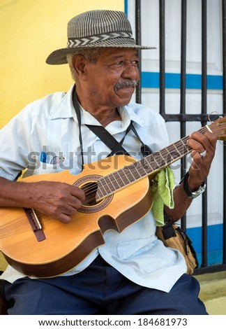 HAVANA, CUBA - FEBRUARY 25, 2014: Street musician playing traditional cuban music on an acoustic guitar for the entertainment of tourists in a typical colorful Old Havana street