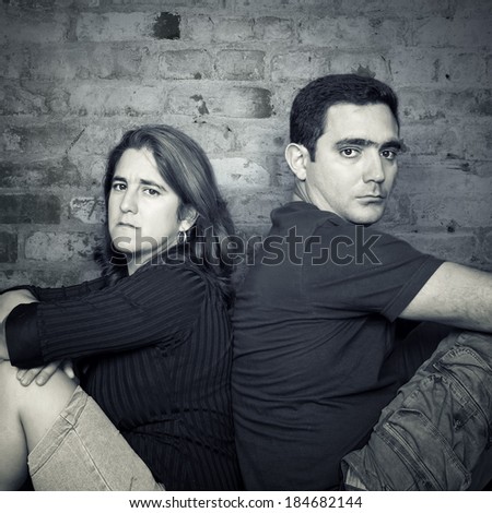 Divorce,problems - Young couple angry at each other sitting back to back with a bricks wall background