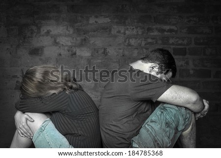 Divorce,problems - Young couple angry at each other sitting back to back with a bricks wall background