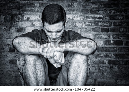 Black and white image of a depressed and lonely young man sitting on the floor with a dirty bricks background