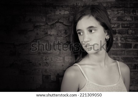 Black and white image of a sad and melancholic teenage girl leaning on a grunge bricks
