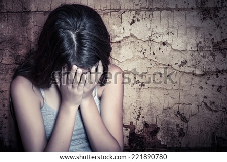Teenage girl crying sitting on the floor with a grunge wall background