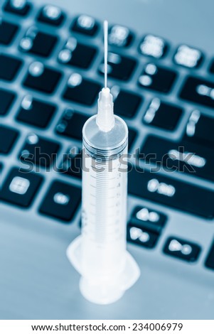 Computer system health - Syringe over a computer keyboard toned in blue