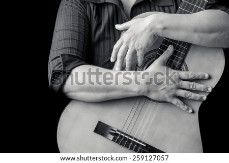 Acoustic guitar detail on black and white - Musician hands playing a classic guitar isolated on a black background