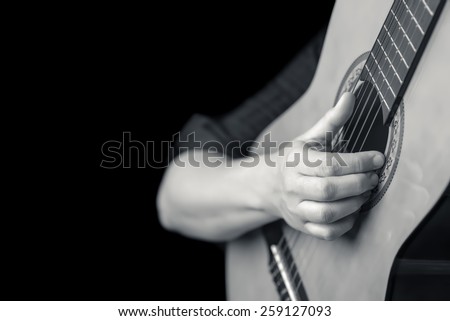Acoustic guitar detail on black and white - Musician hands playing a classic guitar isolated on a black background