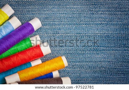 Set of colorful  thread reels creating a frame   on a blue denim fabric with space for text
