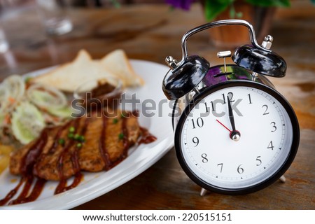 Clock on Wooden Table with steak on background, Lunch Time Concept