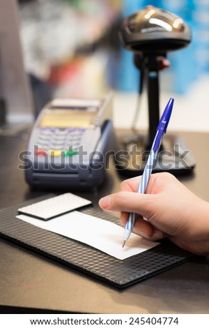 Consumer signing on a sale transaction receipt with Credit Card Machine and Barcode Scanner in Background