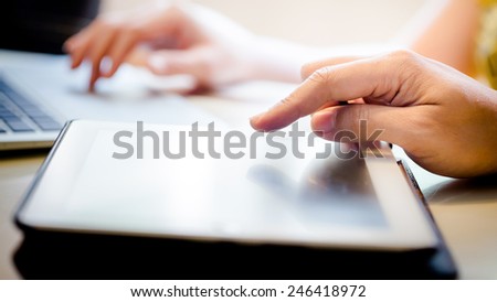 Hand Touching Screen On Modern Digital Tablet PC. Selective focus on finger. With Hand Playing Laptop In Background