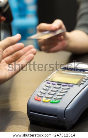 Credit Card Machine on the Table with Woman handing over credit card to Cashier in Background